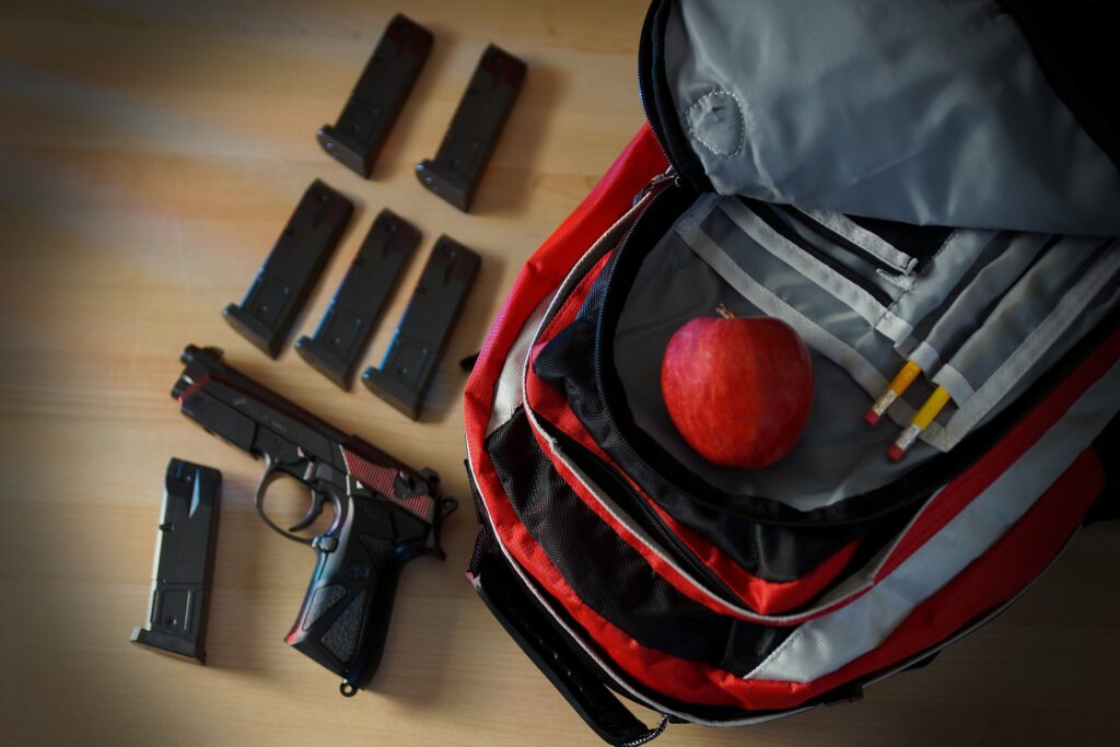 School backpack beside a handgun and ammunition, representing school safety and security risks
